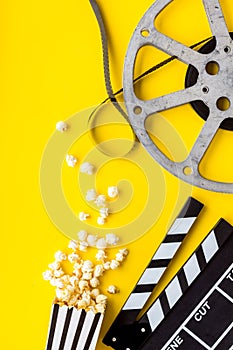 Go to the cinema with popcorn, film type and clapperboard on yellow background top view