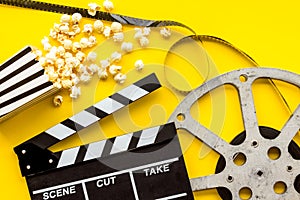 Go to the cinema with popcorn, film type and clapperboard on yellow background top view