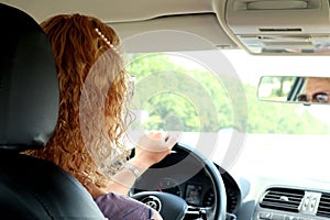 Go on a trip: a young woman with curly hair driving a car, her hand lies on the steering wheel, space for text, close-up