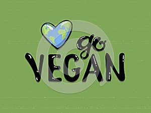 Go vegan lettering on a green background, near a planet earth in the form of a heart . Eco friendly conceptual handwritten phrase.