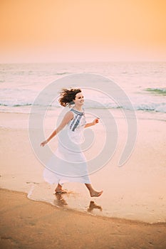 Goa, India. Young Caucasian Woman With Fluttering Hair In Wind In White Dress Walking Along Seashore, Enjoying Life And