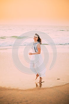Goa, India. Young Caucasian Woman In White Dress Walking Along Seashore, Looking At Camera And Smiling In Summer