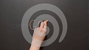 Goal. A left female hand writes the word `GOAL` by orange chalk on a black board. Conceptual chalk drawing
