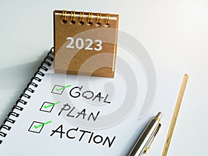 Goal, plan and action, text with checkmarks on notepad with pen and small beige desk calendar on white background.