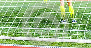 Goalkeeper woman stands against goal with net and stadium.