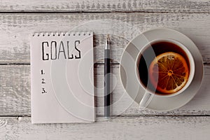 Goals concept. Notebook with goals list, cup of tea on wooden table. Motivation