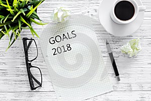 Goals list for 2018. Sheet of paper near pen, glasses and cup of coffee on grey wooden background top view mockup