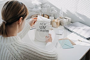 2022 goals, New year resolution. Woman in white sweater writing Text New year resolution in open notepad on the table