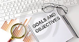 GOALS AND OBJECTIVES text written on a notebook with keyboard, chart,and glasses