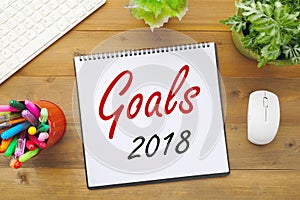 2018 goals on paper note book background on office table, business and new year concept