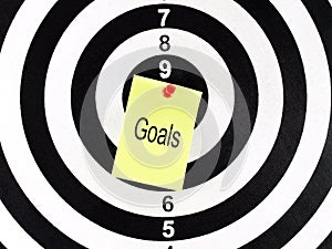 goals word on note paper with red push pin tacking on bullseye target of dartboard