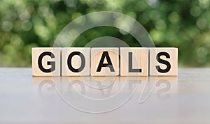 GOALS word written on wooden blocks. The text is written in black letters and is reflected in the mirror surface of the table.