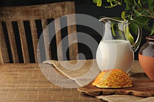 Goat cheese with condiments and jug of milk on wooden table.