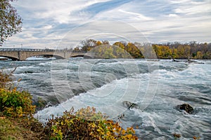 Goat Island Bridge in Niagara Falls State Park, upstream of Niagara Falls waterfall with beautiful autumn leaves foliage sunset,