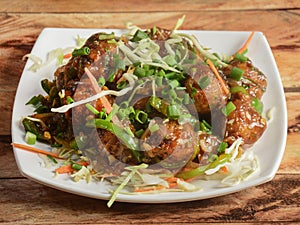 Gobi Manchurian, Popular indo-chinese food made of cauliflower florets, served in a white plate over a rustic wooden table.