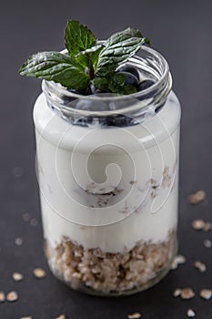 goblet of yogurt with cereals and fruits strewed on leaves mint