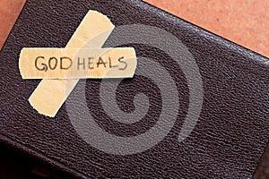 God heals, a handwritten message text on a bandage tape with closed Holy Bible Book with copy space