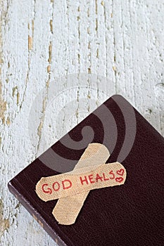 God heals, handwritten text on bandage placed on closed holy bible book