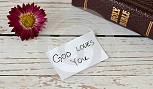 God Jesus Christ loves you handwritten message inspiring quote with closed Holy Bible Book, and flower on wooden background