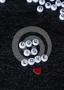 God is love text written with round letter beads and red paper heart on black background