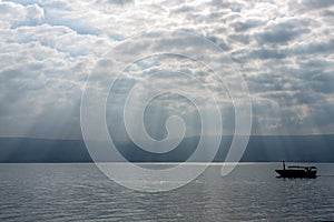 God`s rays over the Sea of Galilee with boats in silhouette.