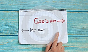 God`s way, message quote on a notebook with a hand showing in direction to handwritten arrow isolated on a blue wooden background