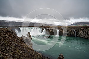 Godafoss waterfall near Akureyri in the Icelandic highlands. Dramatic clouds and snow covered mountains in the back.