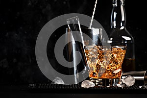 Godfather alcoholic cocktail with scotch whiskey, amaretto liqueur and ice. Black bar counter background, steel bar tools, copy