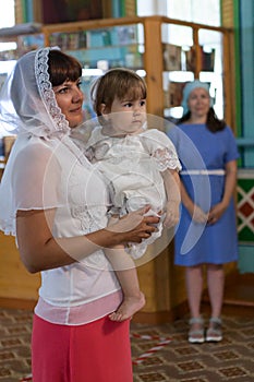 Godmother with godchild stand in the Orthodox church. Mother stands on the side. Ceremony of sacrament of initiation into the