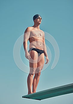 Going for gold. Full length shot of a handsome young male athlete standing on a diving board outside.