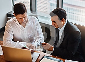 Going into partnership is the right solution for you. two businessmen having a discussion while sitting by a laptop.