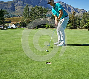 This is going straight in. a focused young man hitting a golfball with a putter into a hole on a golf course.