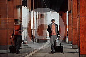 Going to airport terminal. Confident businessman traveler walking on city streets and pulling his suitcase drinking