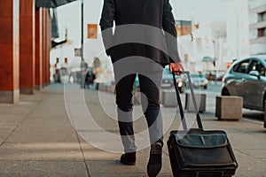 Going to airport terminal. Confident businessman traveler walking on city streets and pulling his suitcase drinking