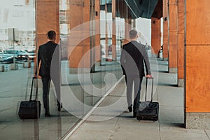 Going to airport terminal. Confident businessman traveler walking on city streets and pulling his suitcase drinking