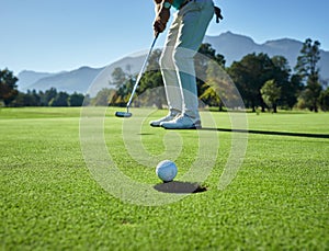 This is going to be in. Low angle shot of a unrecognizable man hitting a golfball into a hole on a golf course.