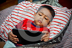 Before going to sleep a child is lying a homemade hammock and watching cartoons using a smartphone.