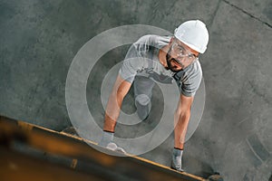 Going up on the ladder, top view. Young factory worker in grey uniform