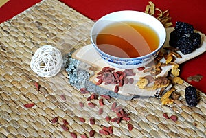 Goji berries, chinese dates, astragalus root pieces with a bowl of herb tea on red background. Side view.