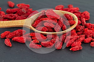 Goji berries close up dried red berry in wooden spoon on grey slate plate