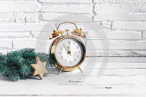 Gold alarm clock, green spruce branch and golden star. Christmas and New Year composition. White wood table, brick backdrop.