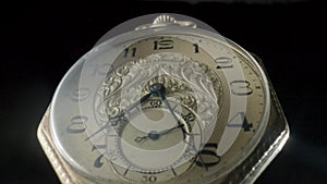 Gold antique pocket watch on a stand rotating on a black isolated background. Round golden retro clock with a white dial