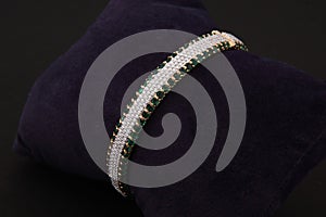 gold bangle jewelry with white and green diamonds isolated on brown background