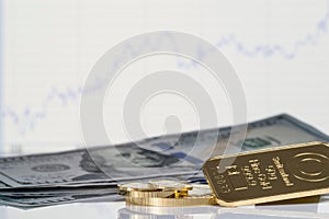 Gold bar, coins and a hundred-dollar bills on the background of the growth chart