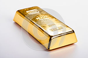 Gold bar rests on white backdrop. Engravings indicate weight, purity. Light reflects off surface, emphasizing value, quality