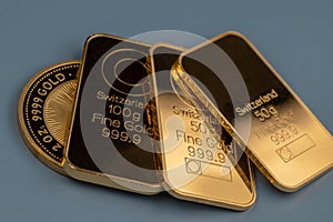 Gold bars and gold coin on a blue grey background