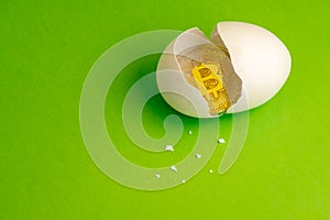 Gold Bitcoin coin in a broken egg. White eggshell with cryptocurrency symbol inside instead of yolk. Green background. Copy space