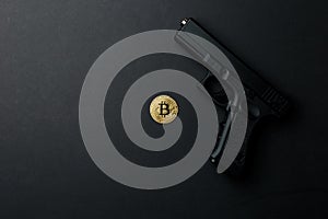 A gold bitcoin coin next to a gun on a black background. Bitcoin Conservation. Cryptocurrency. Close-up