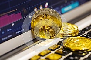 Gold bitcoin on the laptop keyboard on the background of the stock chart