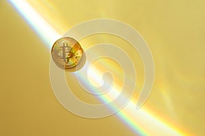 Gold bitcoin on a yellow background with a rainbow, copy space.